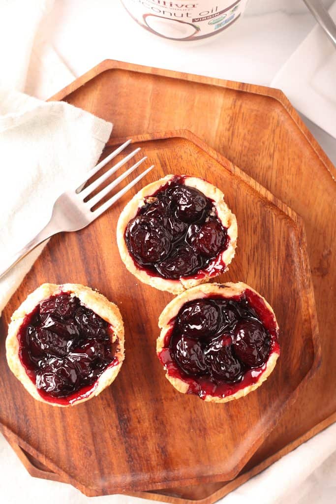 overhead shot of three vegan mini cherry pies on an octagonal wooden plate with a silver fork