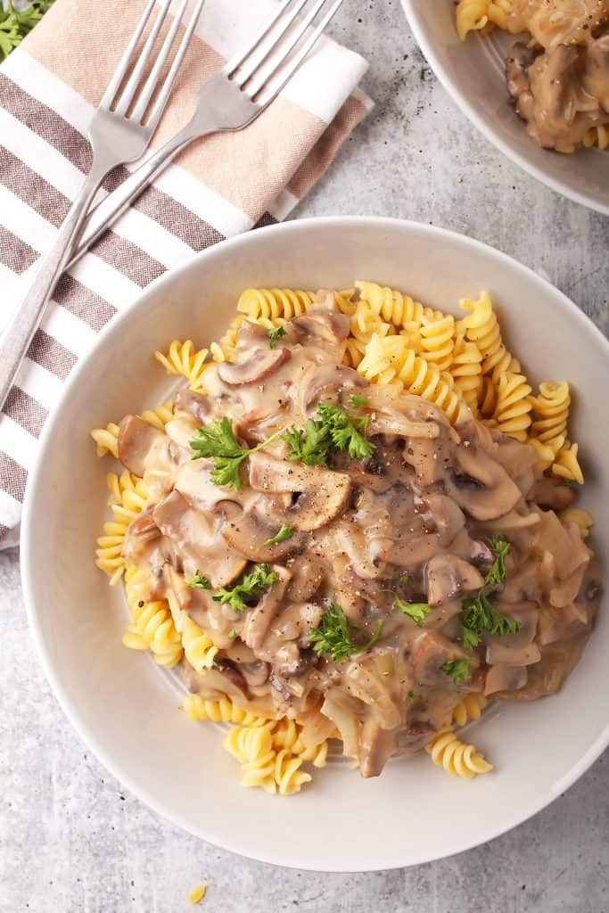 overhead shot of vegan mushroom stroganoff over rotini pasta in a white bowl on a grey table