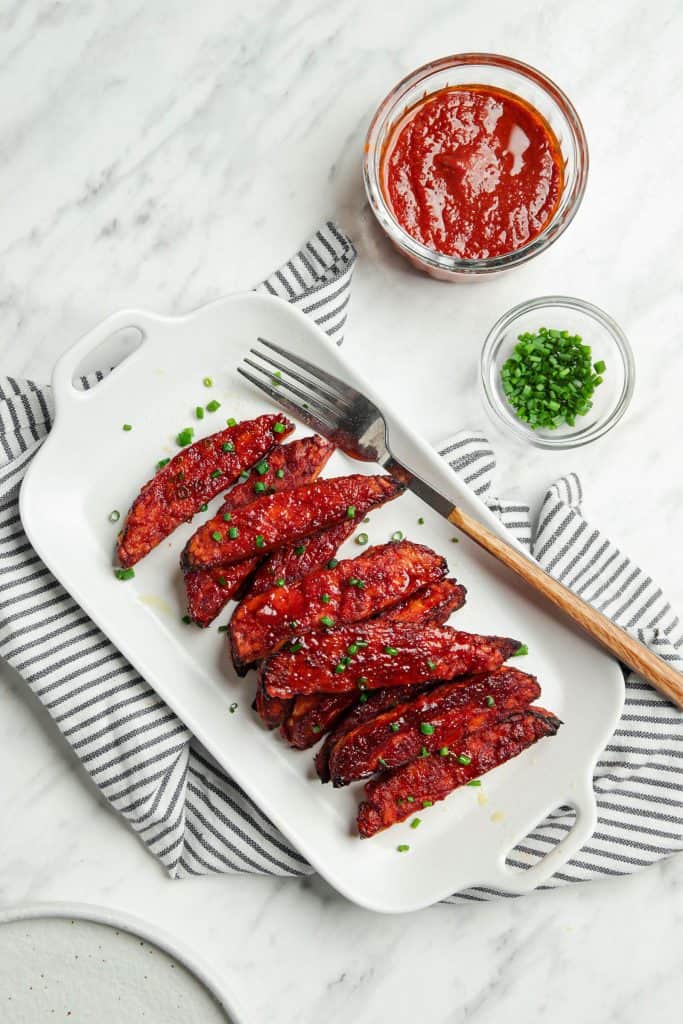 Vegan ribs made with tempeh served on a white plate with a fork and green onions