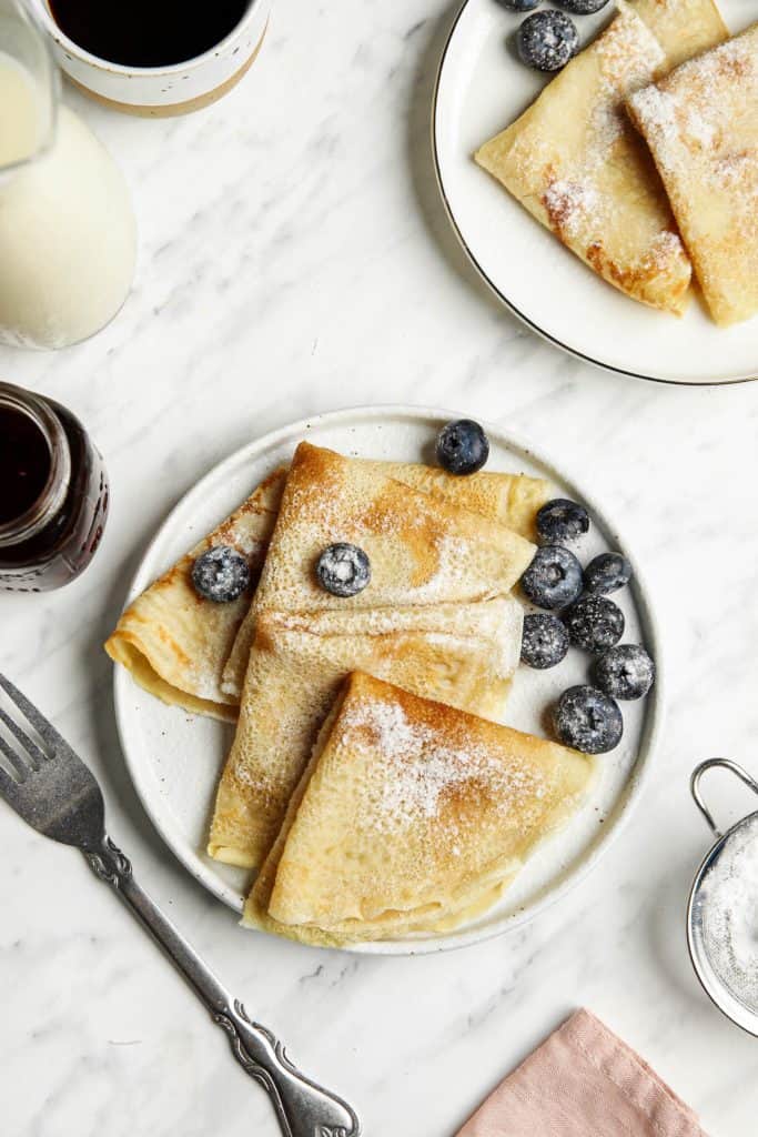 Best-ever vegan crepes on a plate served with powdered sugar and blueberries