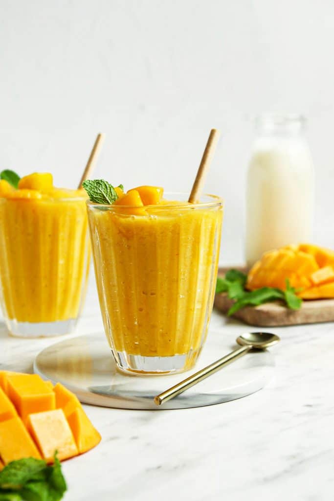 Finished mango smoothie in two glasses topped with fresh mango and mint. 