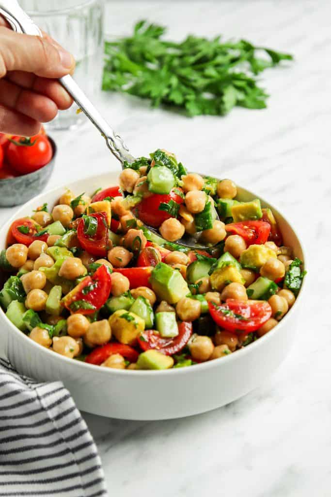 front view of Greek chickpea salad in white bowl with spoon