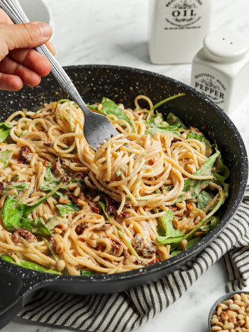 one pan filled with pasta, hummus, and arugula