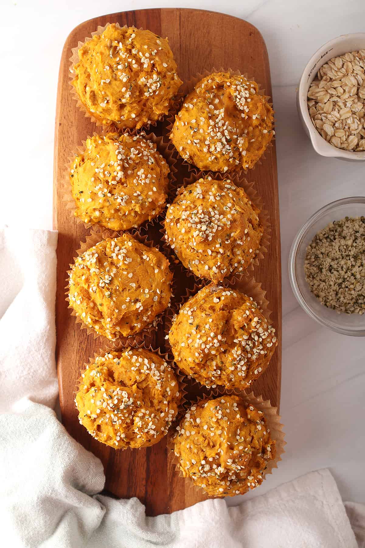 8 healthy pumpkin hemp muffins on a wooden cutting board with two off to the side on a white tabletop