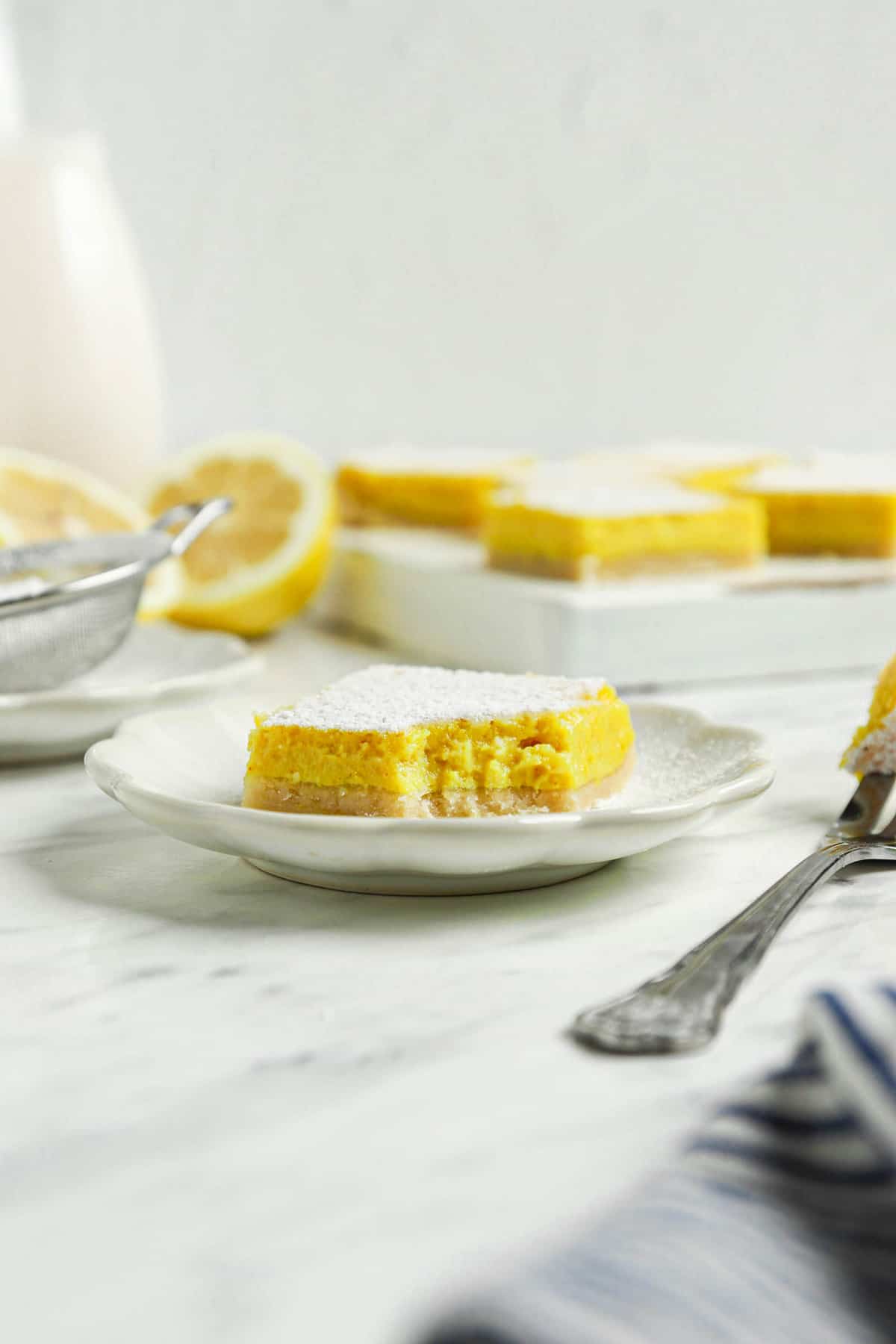 one vegan lemon bar on white plate with sugar