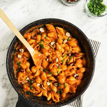 top view of pumpkin pasta with alfredo in skillet with spoon spoon and two bowls of hazelnuts and green onions