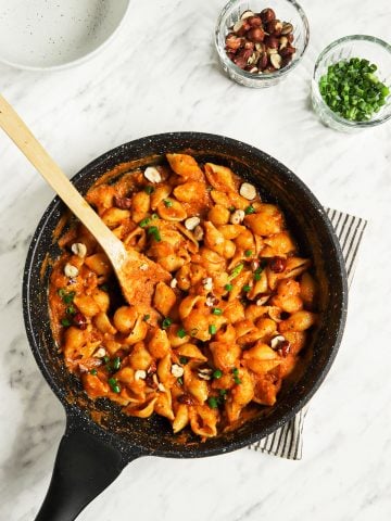 top view of pumpkin pasta with alfredo in skillet with spoon spoon and two bowls of hazelnuts and green onions