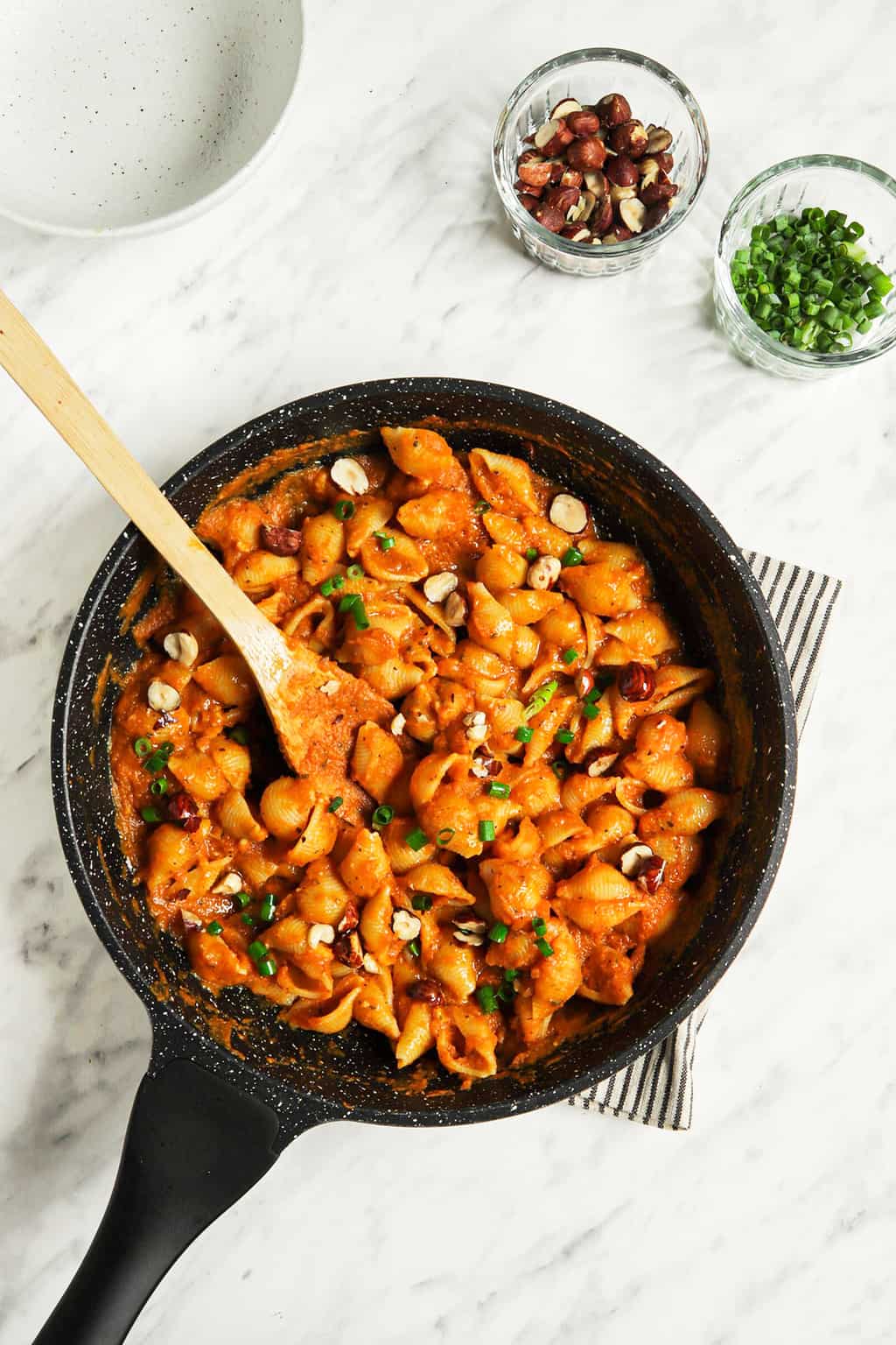 top view of pasta and alfredo sauce made with pumpkin and dairy-free milk in black skillet with chives and wooden spoon 