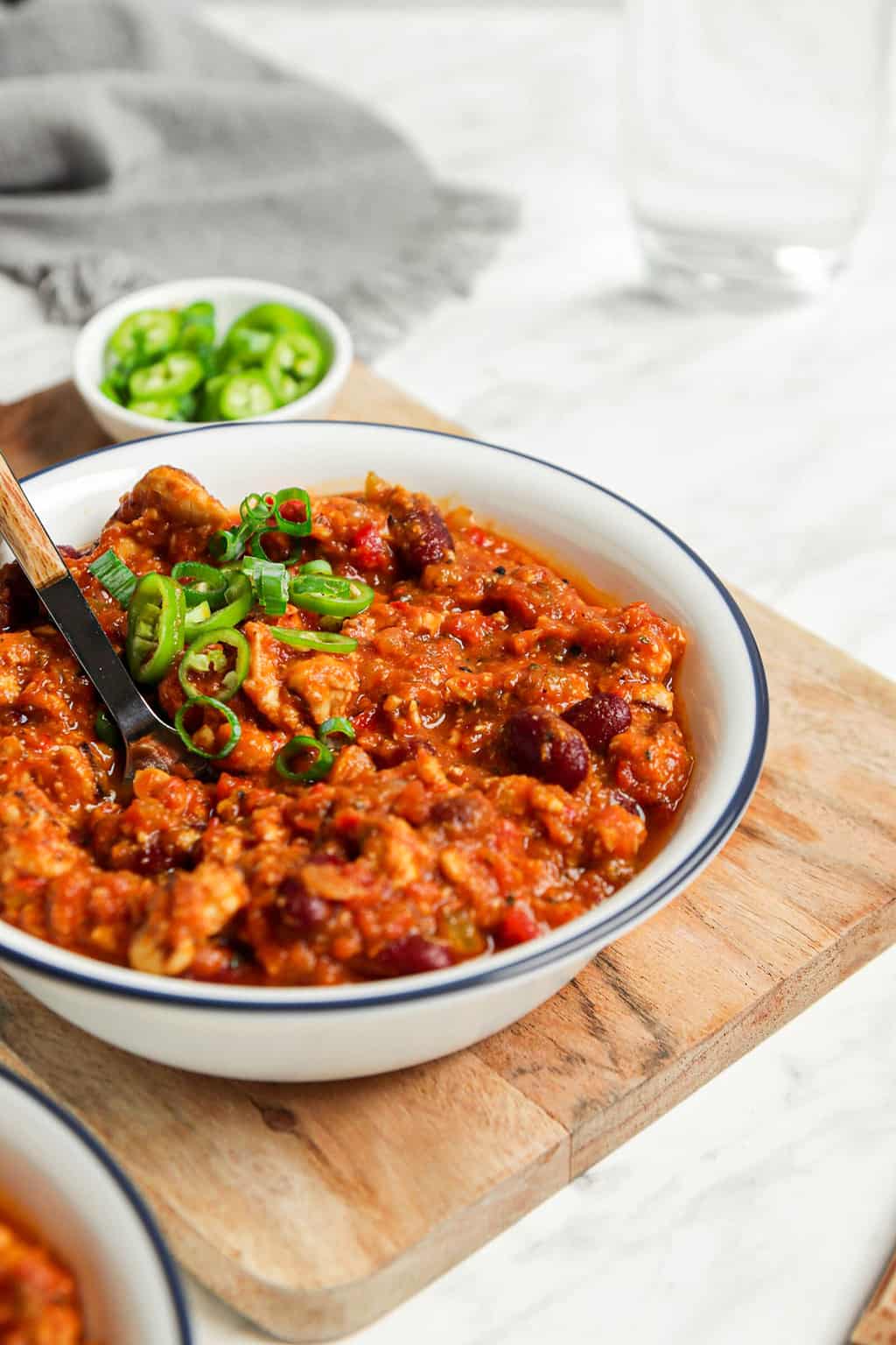 gluten-free vegan pumpkin chili in white bowl with sliced green onions on wooden serving board with utensil in bowl 