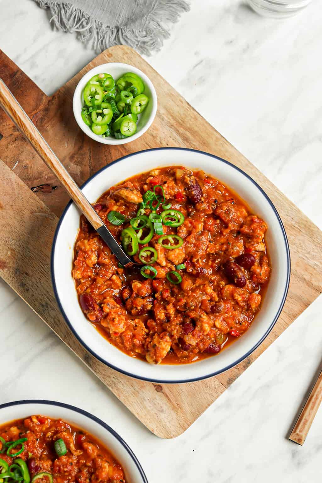 one white bowl filled with vegan gluten-free pumpkin chili on wooden board. Topped with sliced green onions