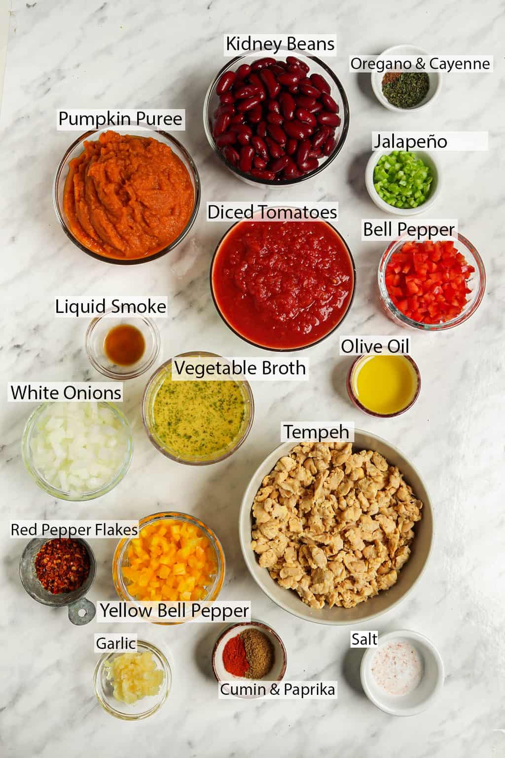 ingredients shot of gluten-free vegan pumpkin chili featuring kidney beans, oregano, cayenne, jalapeño, pumpkin puree, tomatoes, liquid smoke, olive oil, vegetable broth, white onions, tempeh, red pepper flakes, yellow bell pepper, garlic, salt, cumin, paprika, 