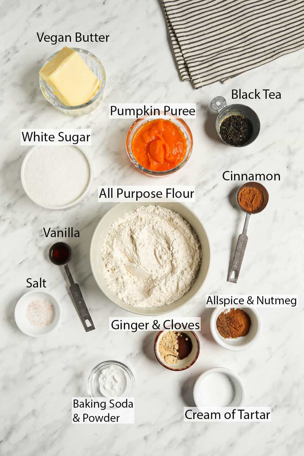 ingredients shot with linen including vegan butter, pumpkin puree, black tea, granulated sugar, all-purpose flour, cinnamon, vanilla, salt, ginger, cloves, allspice, nutmeg, baking soda and powder, and cream of tartar