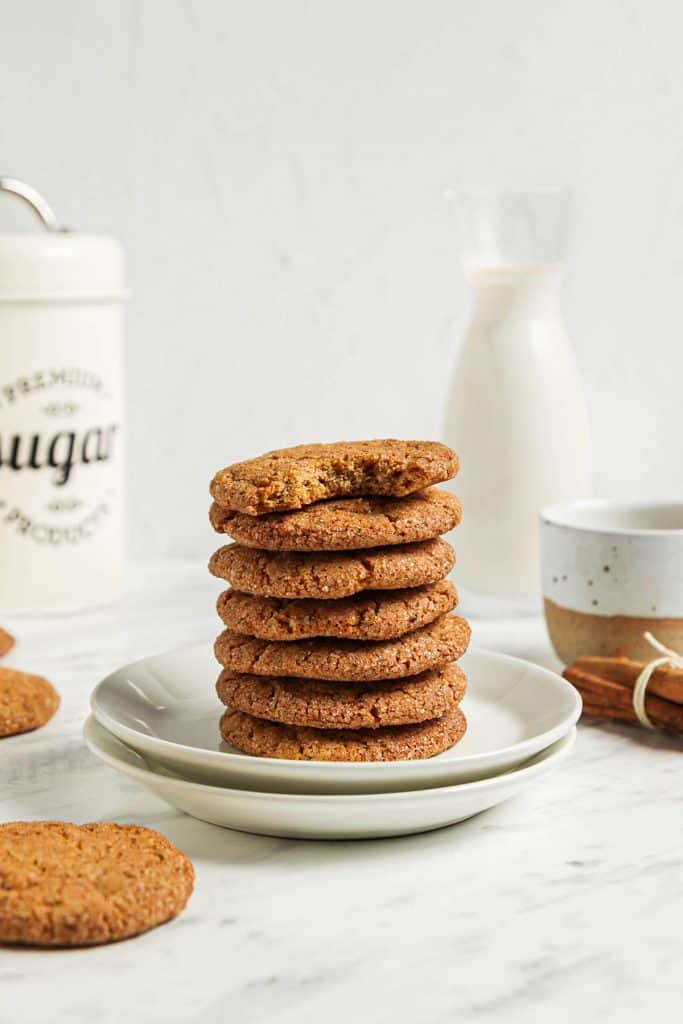 stack of seven pumpkin snickerdoodle cookies on two white plates with cinnamon and milk in background