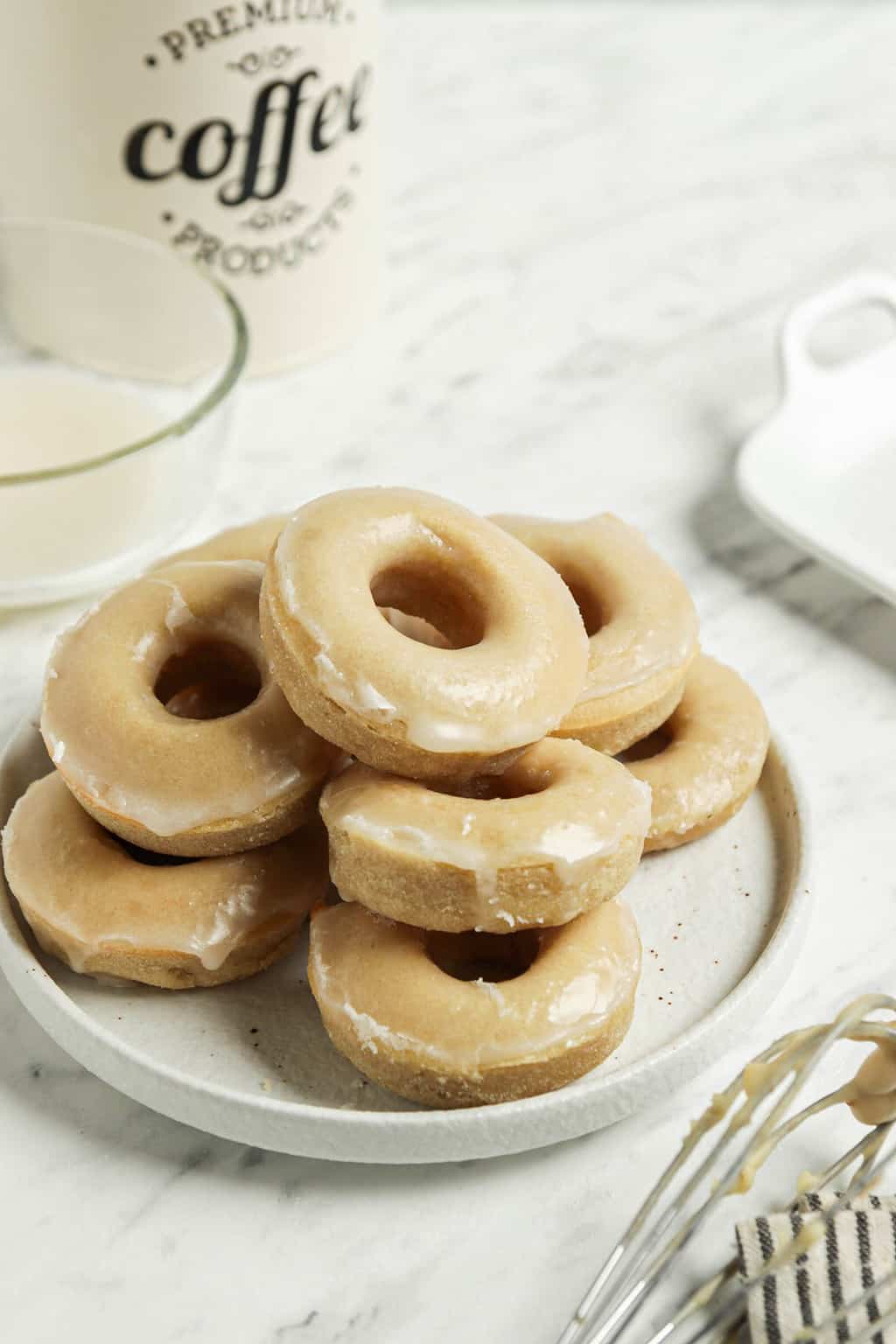 one plate filled with a group of glazed doughnuts from the vegan donut recipe ready to be eaten. One tin of coffee in the background 