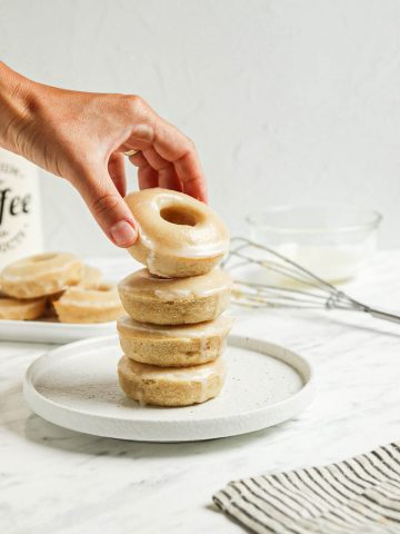 one stack of vegan glazed donuts on white plate with hand