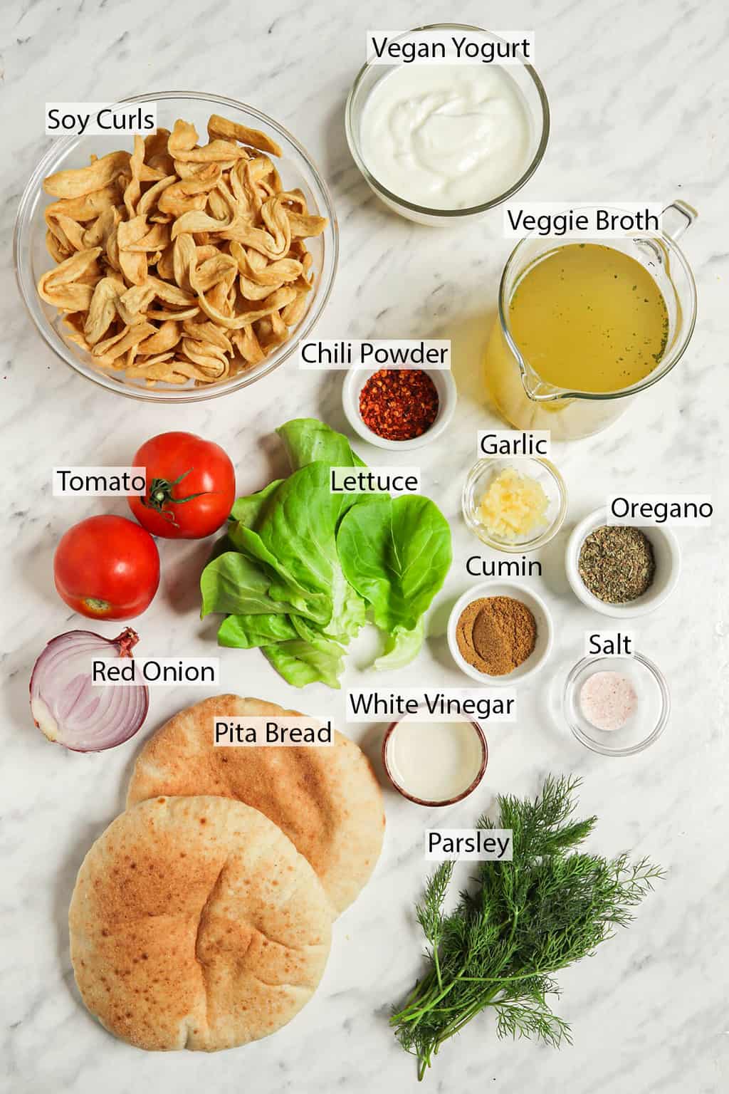 recipe ingredients for homemade vegan gyros such as vegan yogurt, soy curls, veggie broth, chili powder, garlic, oregano, tomatoes, lettuce, cumin, vinegar, salt, red onion, pita bread, dill 