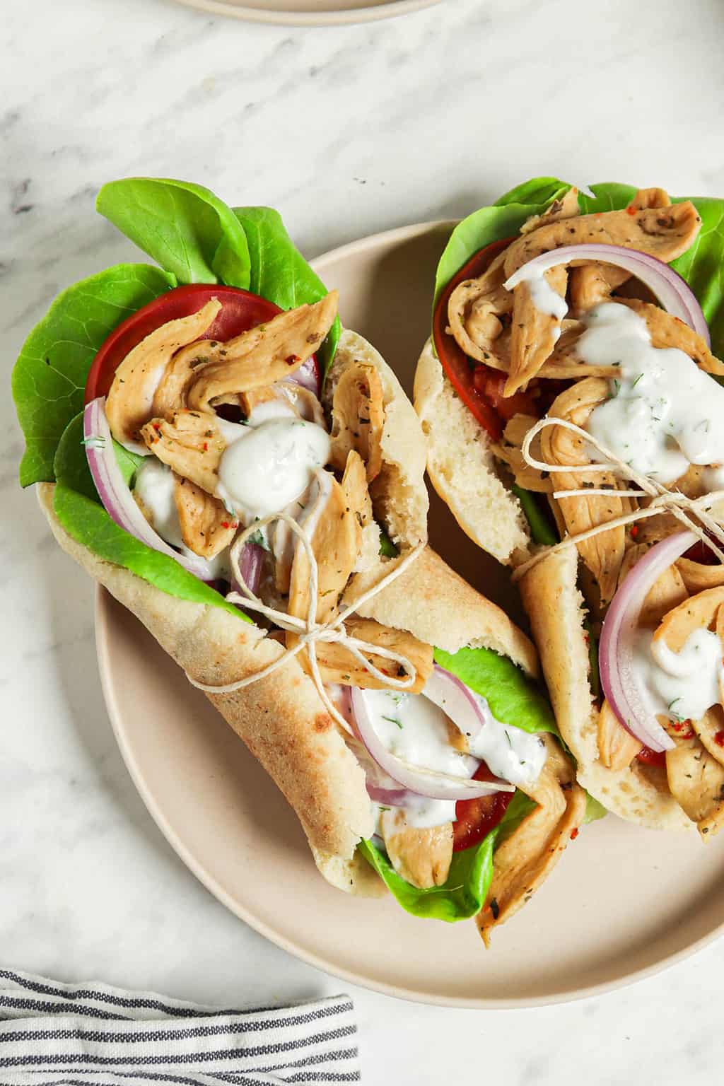 one close image of two vegan homemade gyros on white plate with lettuce, tzatziki sauce, and soy curls