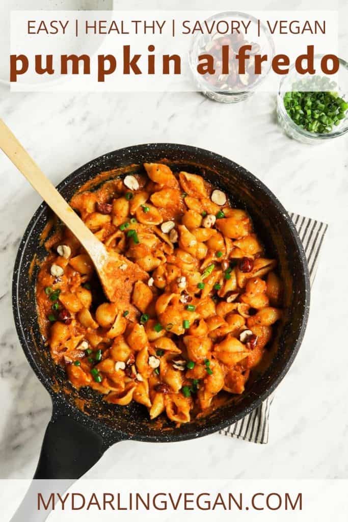 top view of alfredo in skillet with pumpkin and pasta and spoon paired with wooden spoon