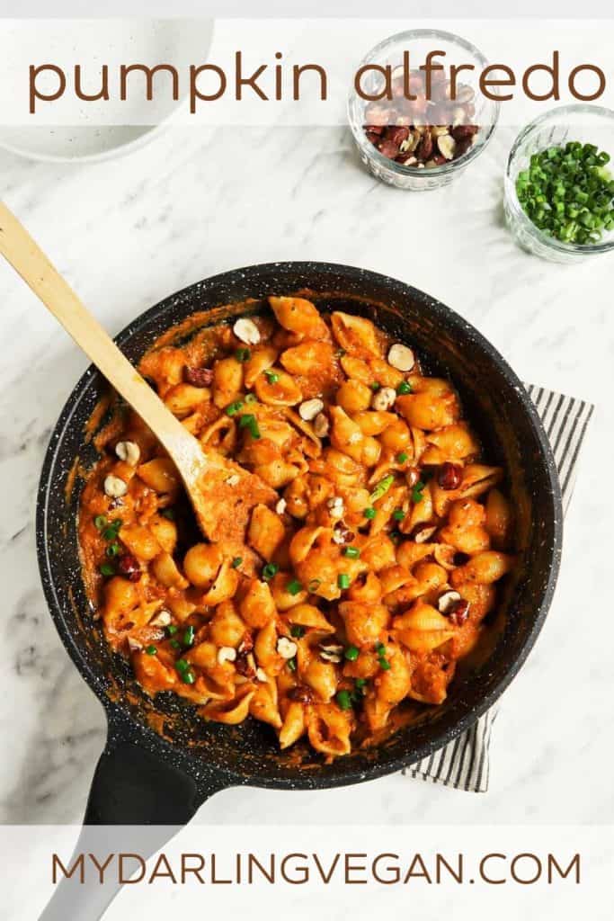 top view of skillet with pumpkin alfredo and pasta with wooden spoon and hazelnuts with green onions