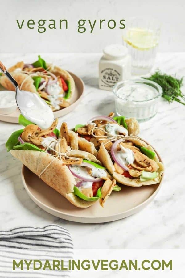 front view of tzatziki sauce being poured over gyro sandwiches on plate