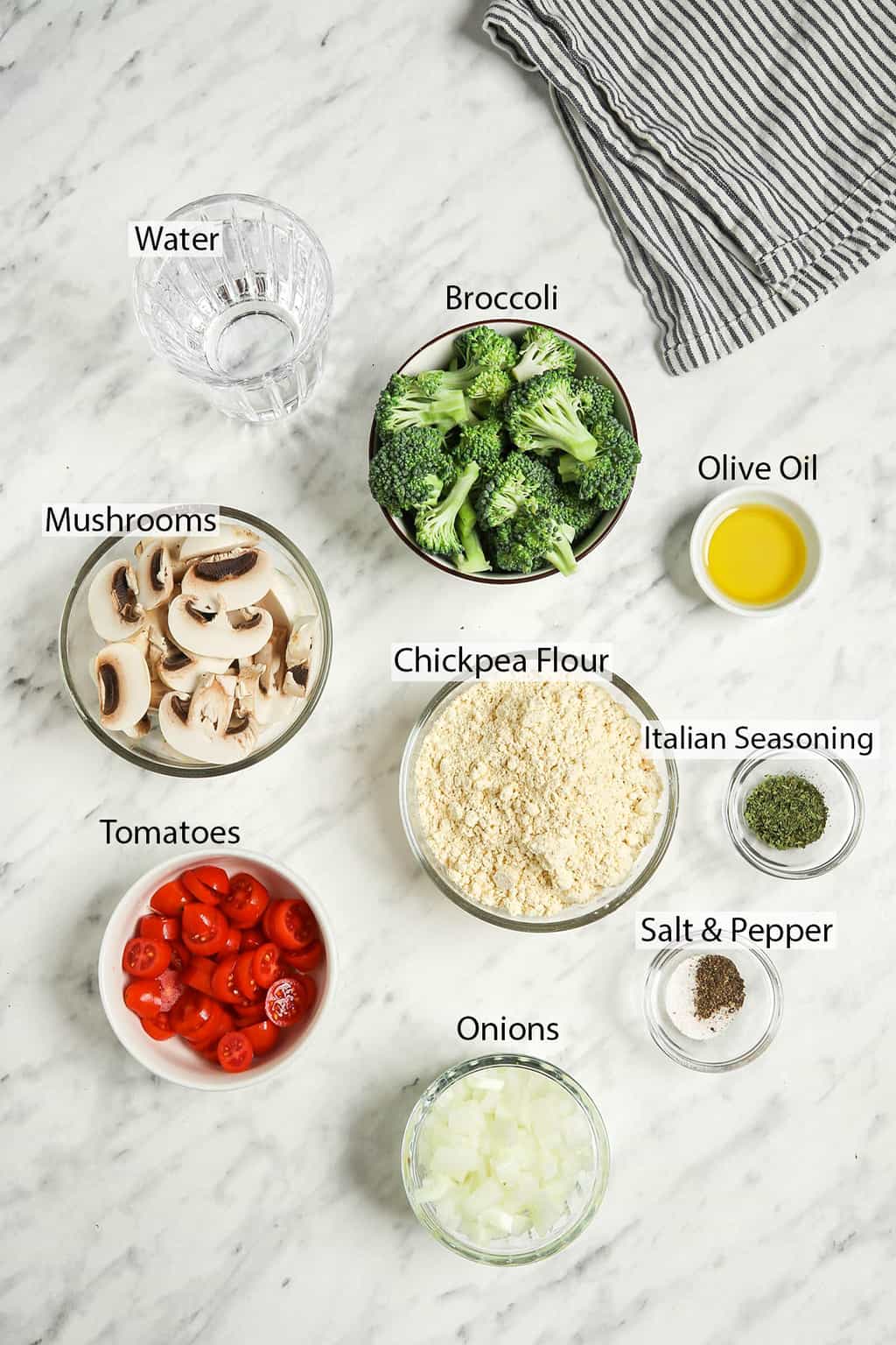 broccoli, olive oil, chickpea flour, mushrooms, tomatoes, onions, salt, pepper, Italian seasoning, and water in bowls for casserole