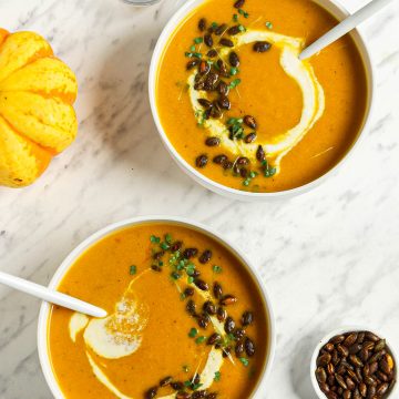 top view of pumpkin curry soup recipe in two bowls with toasted pumpkin seeds and cashew cream