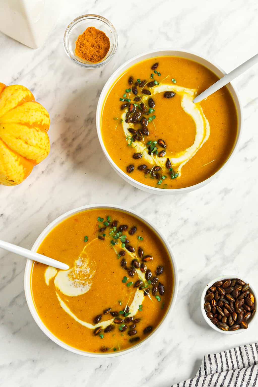 two bowls of pumpkin curry soup with cashew cream and toasted pumpkin seeds. 