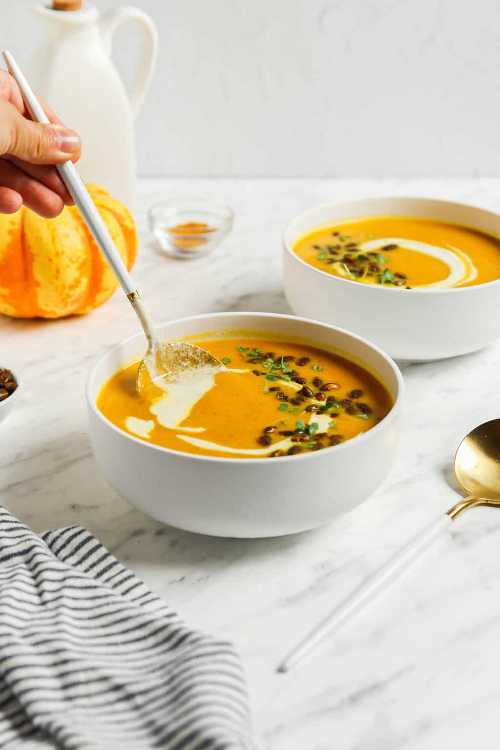 two bowls of vegan pumpkin curry soup topped with toasted pumpkin seeds and creamy cashew creme 