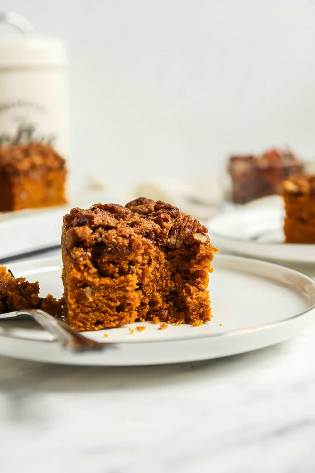 Finished coffee cake on a white plate with a fork and a bite taken out