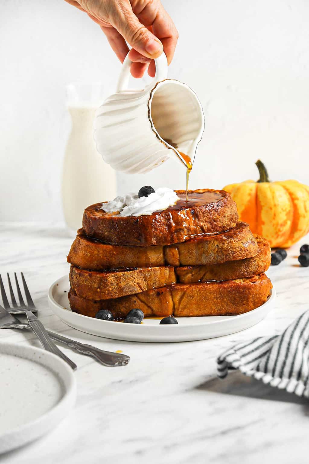 Stack of pumpkin french toast on a white plate with coconut whipped cream and maple syrup. 
