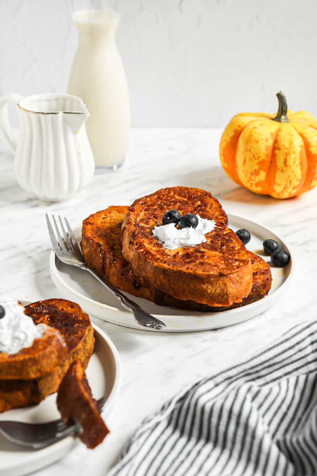 Two pieces of vegan French toast on a white plate with coconut whipped cream and blueberries