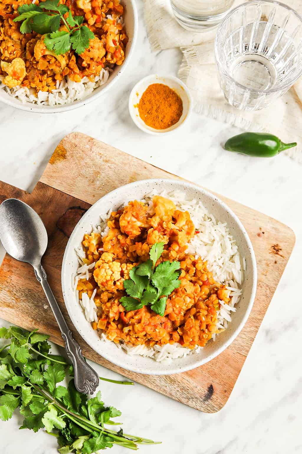Red lentil cauliflower curry served over rice in a white bowl. 
