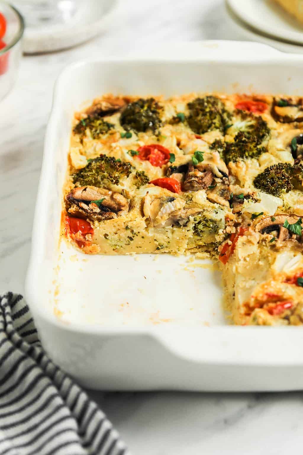 vegan breakfast casserole in white dish with broccoli, tomatoes, onions, and mushrooms 