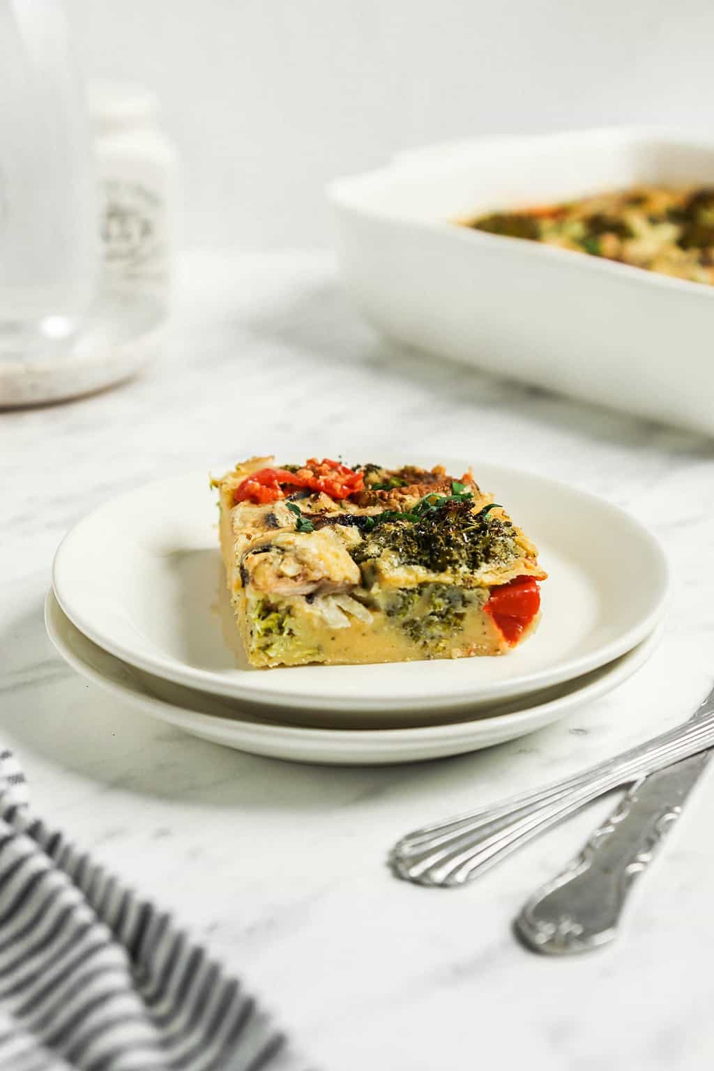 one slice of vegan breakfast broccoli casserole on white plate with silverware to the side 