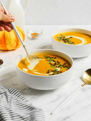 two bowls of pumpkin curry soup with pumpkin seeds and spoon