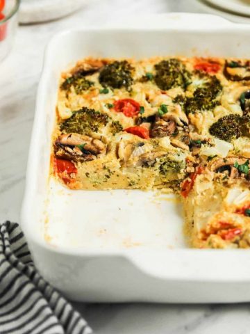 vegan egg bake in white baking dish with broccoli, tomatoes, onion, and mushrooms