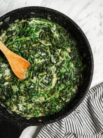 one large skillet with vegan creamed spinach recipe with wooden spoon