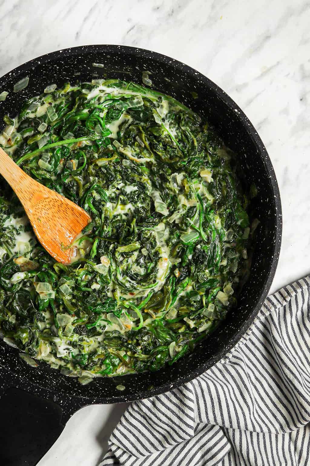 cooked creamed spinach in skillet with wooden spoon