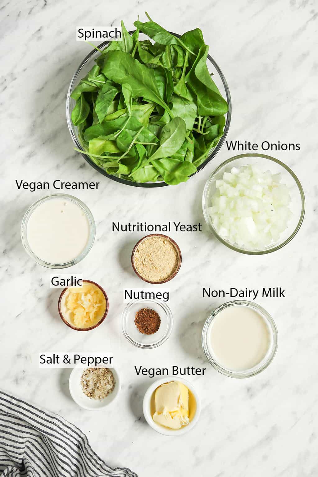 fresh spinach, onions, vegan creamer, nutritional yeast, garlic, nutmeg, non-dairy milk, vegan butter, salt, and pepper in bowls for creamed spinach recipe