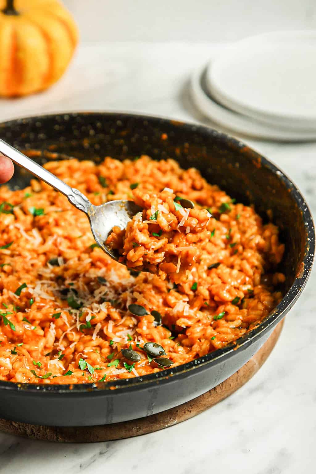 Finished pumpkin risotto in a black skillet with a large serving spoon. 