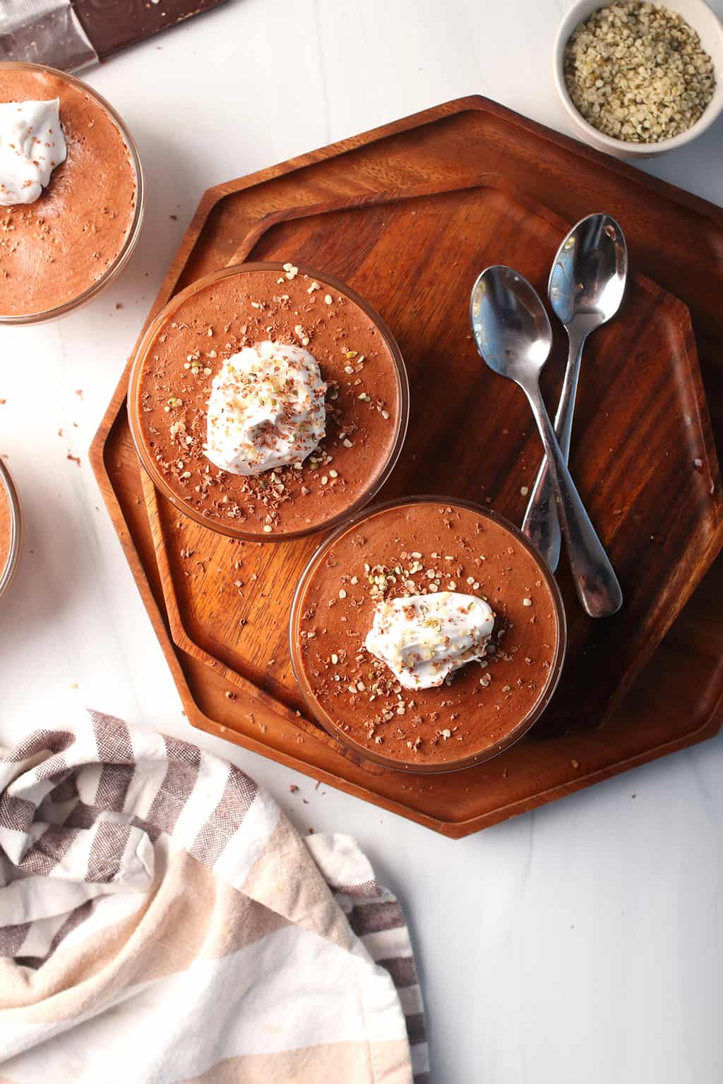 Two finished cups of vegan chocolate mousse on a wooden platter