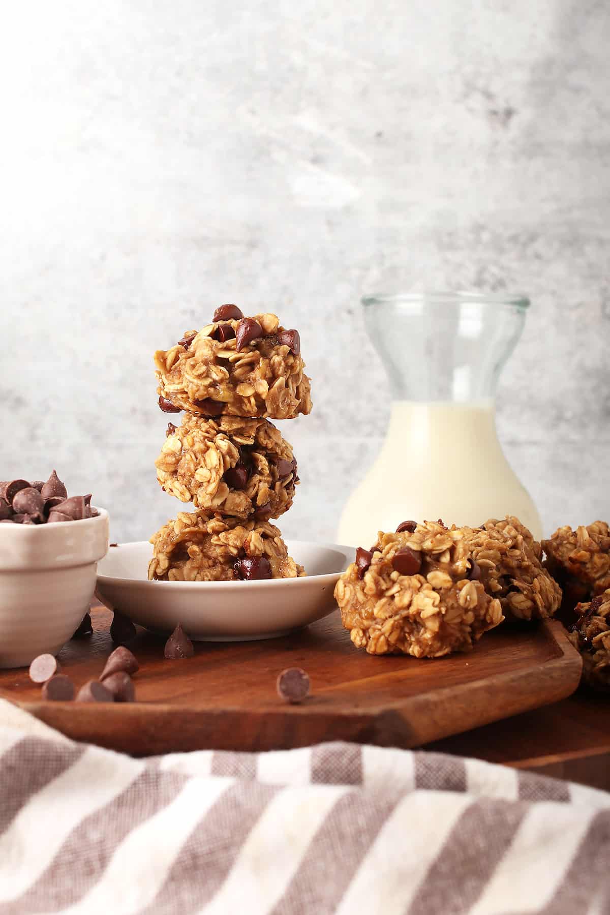 Finished heathy vegan cookies stacked in a small white dish with a jar of milk in the background.