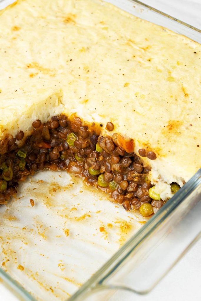 Overhead view of plant-based shepherd's pie in baking dish with a serving removed exposing lentils