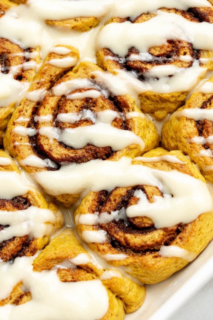extreme close-up of soft vegan pumpkin cinnamon rolls covered in warm maple cream cheese glaze