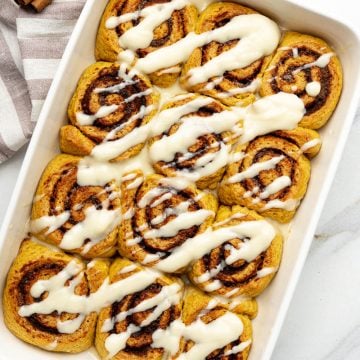 top-down view of warm vegan pumpkin cinnamon rolls in a white baking dish drizzled with creamy maple glaze
