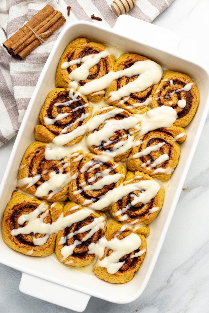 top-down view of warm vegan pumpkin cinnamon rolls in a white baking dish drizzled with creamy maple glaze