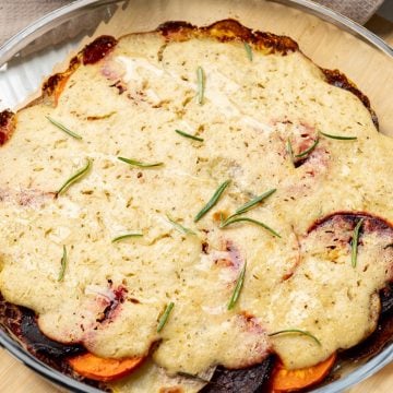 finished vegan vegetable gratin in a glass dish topped with cashew cream and fresh rosemary