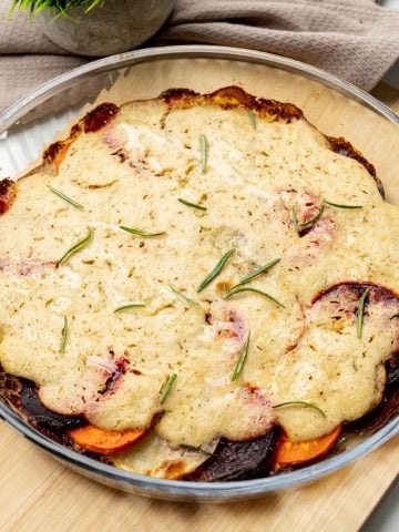 finished vegan vegetable gratin in a glass dish topped with cashew cream and fresh rosemary