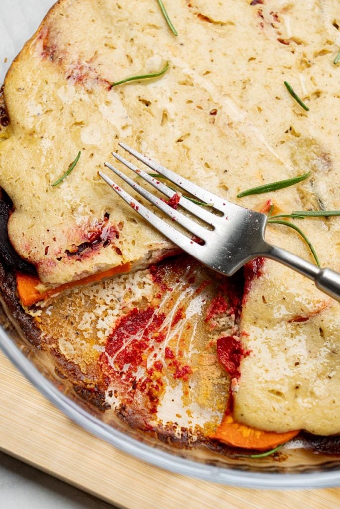 serving root vegetable gratin with a fork exposing layers of beets, carrots and potatoes