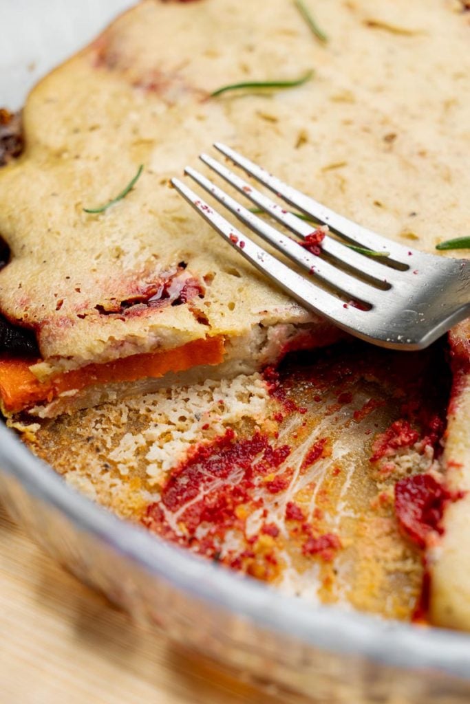 Vegan vegetable gratin with a slice removed showing inner layers of beets, potatoes, and carrots
